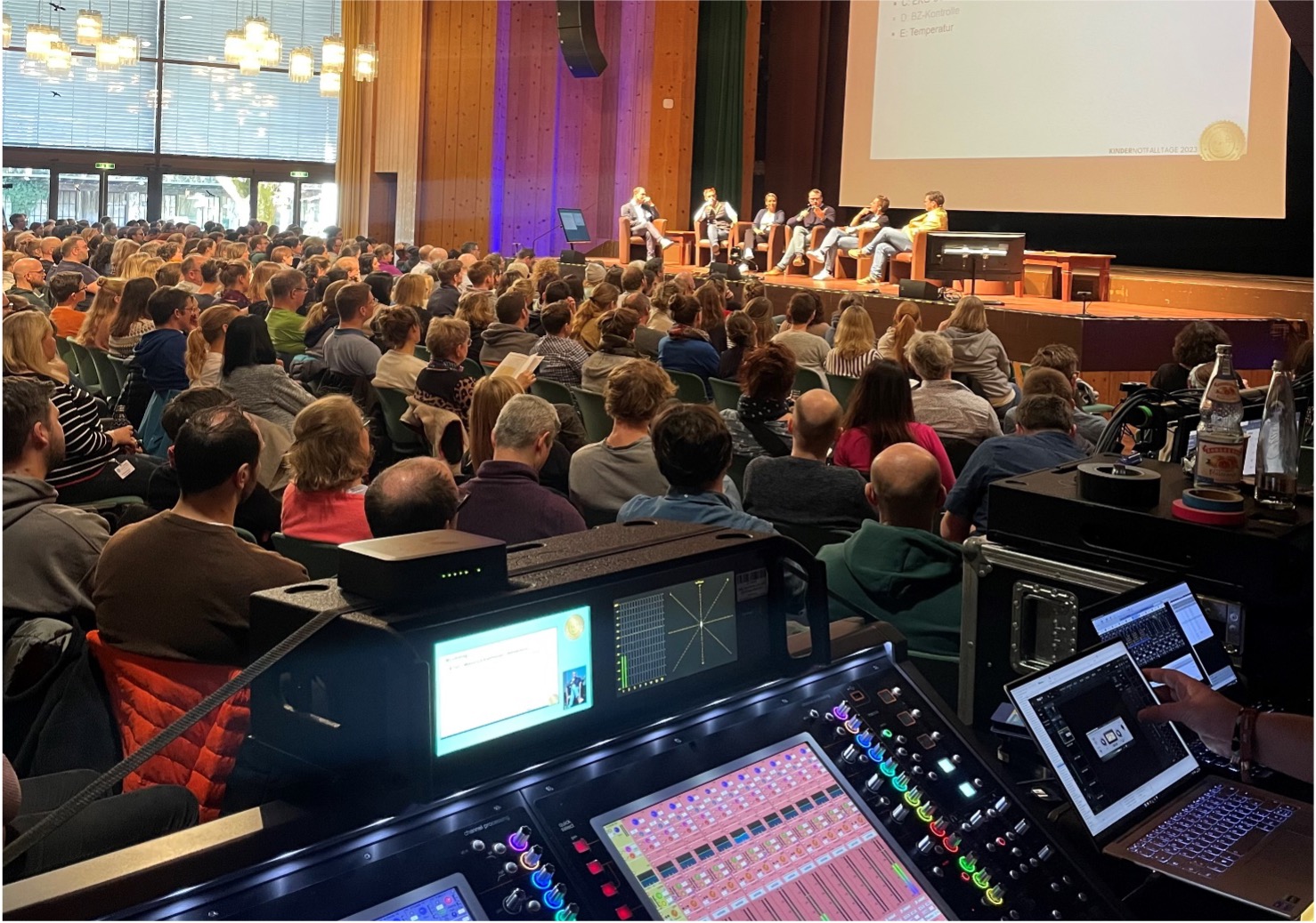 Blick über ein Tonmischpult in einen voll besetzten Kongresssaal bei einem medizinischen Kongress.
